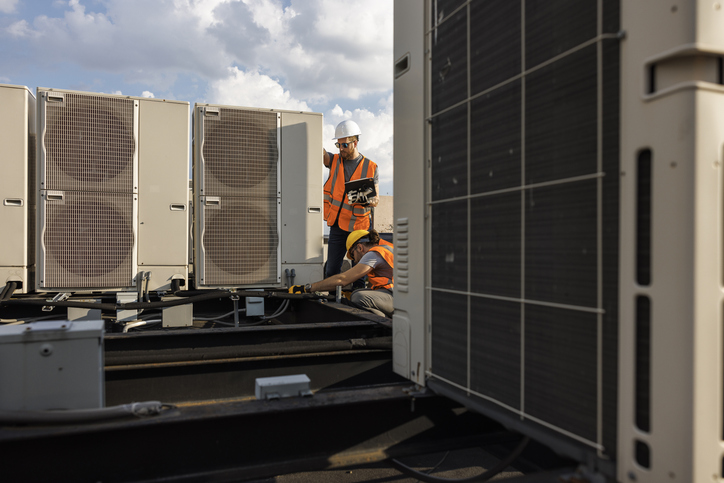 Rooftop air conditioning system inspection. Caucasian white workers check units and log the result with a portable computer.